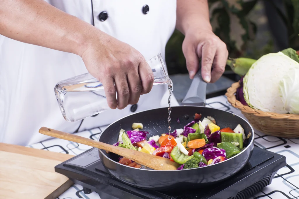 Chef che inserisce l'acqua di Ristoacqua in una padella mentre cuoce alimenti vegetali
